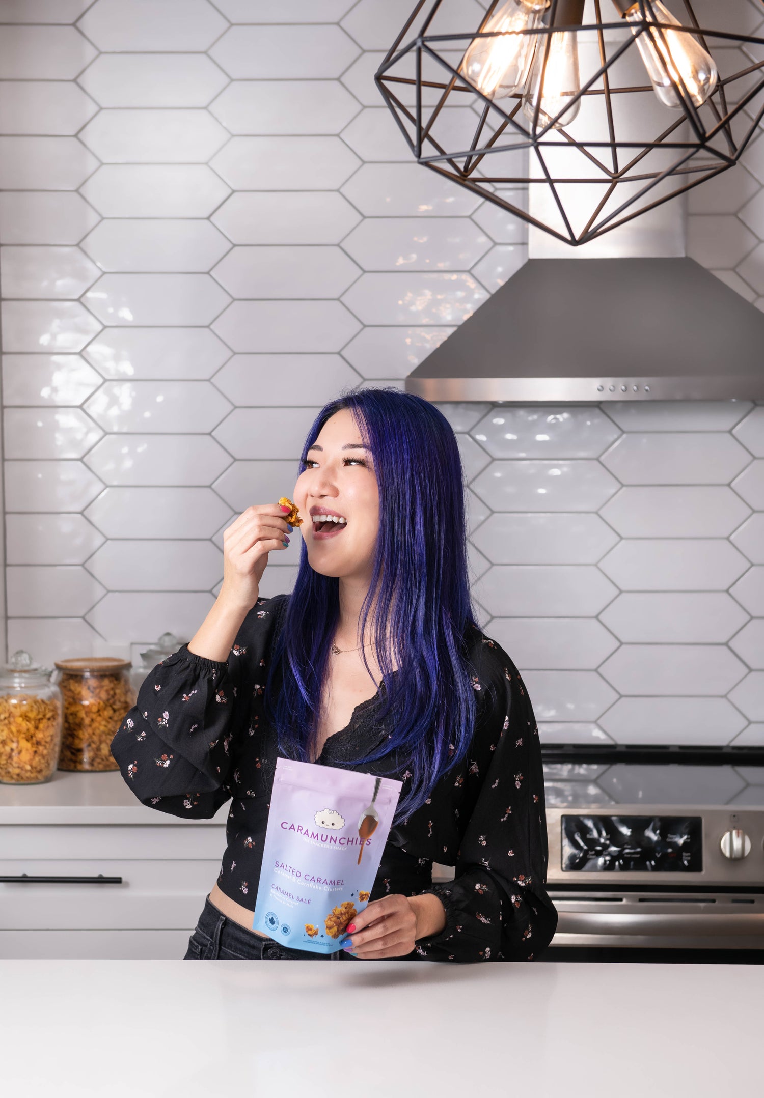 Alysia in a kitchen, with a bag of Salted Caramel Caramunchies, looking to the side while she eats a piece.