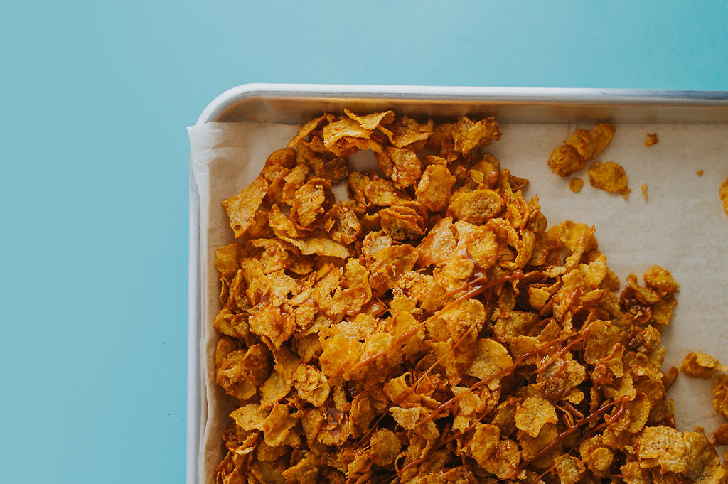 Tray of caramel cornflake clusters with a drizzle of caramel on top on an aqua background