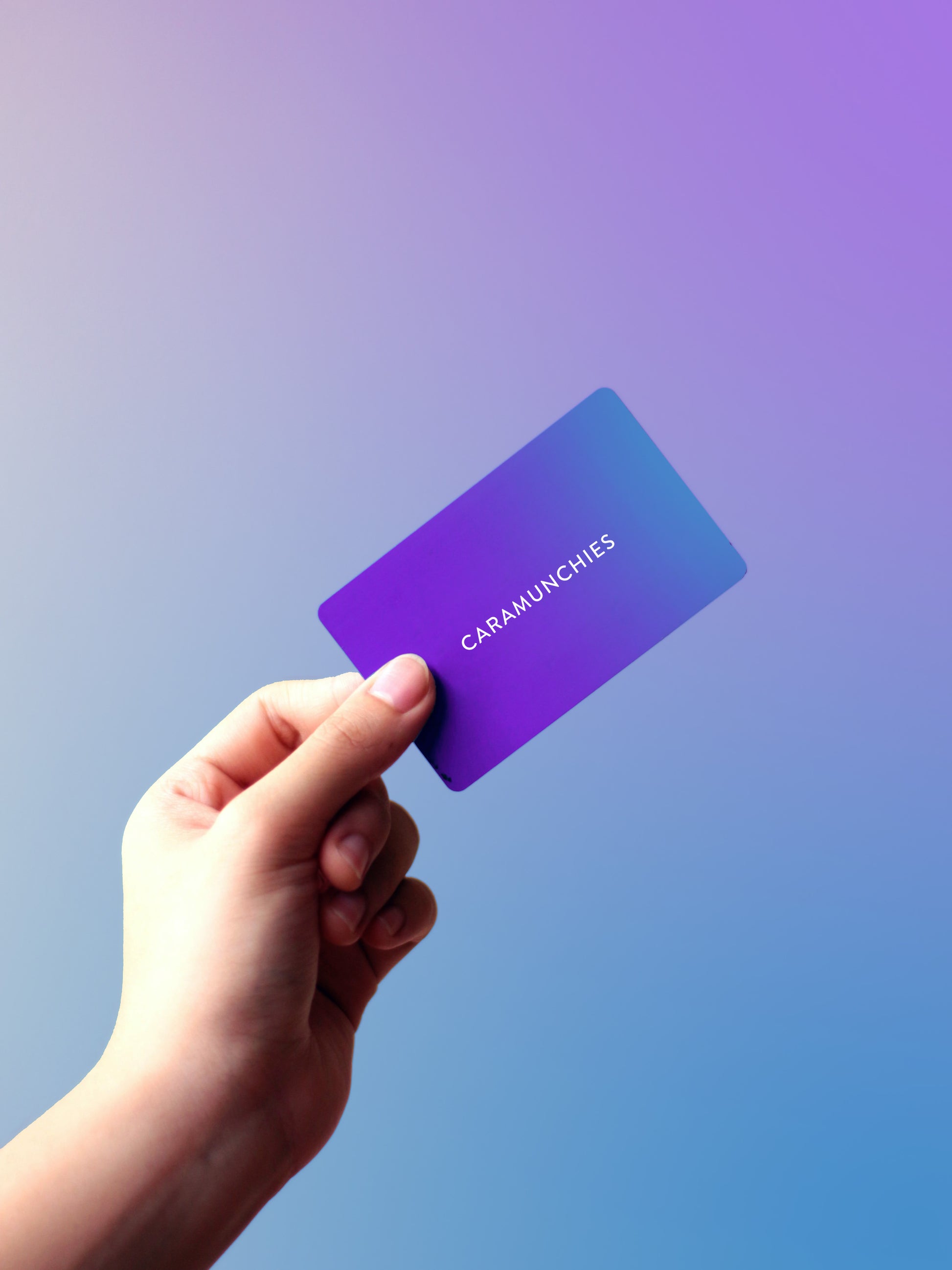 Hand holding a gift card that reads "CARAMUNCHIES" on a purple and blue gradient.