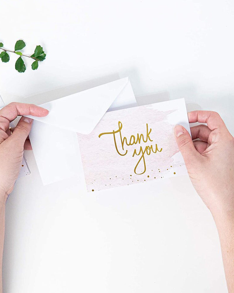 Hands holding a pink "Thank You" card with a white envelope.